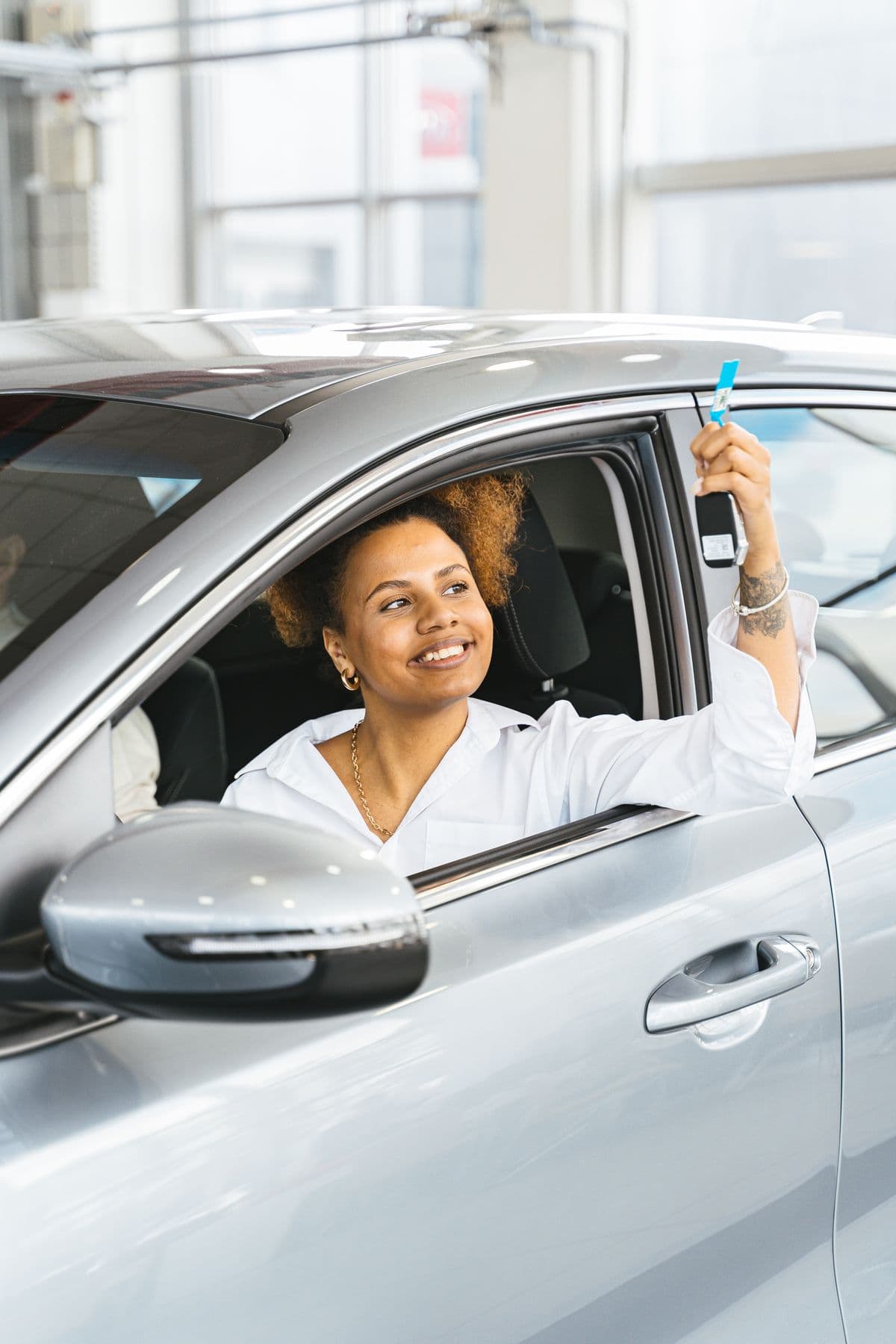 A young woman in the driver's seat holding up car keys triumphantly
